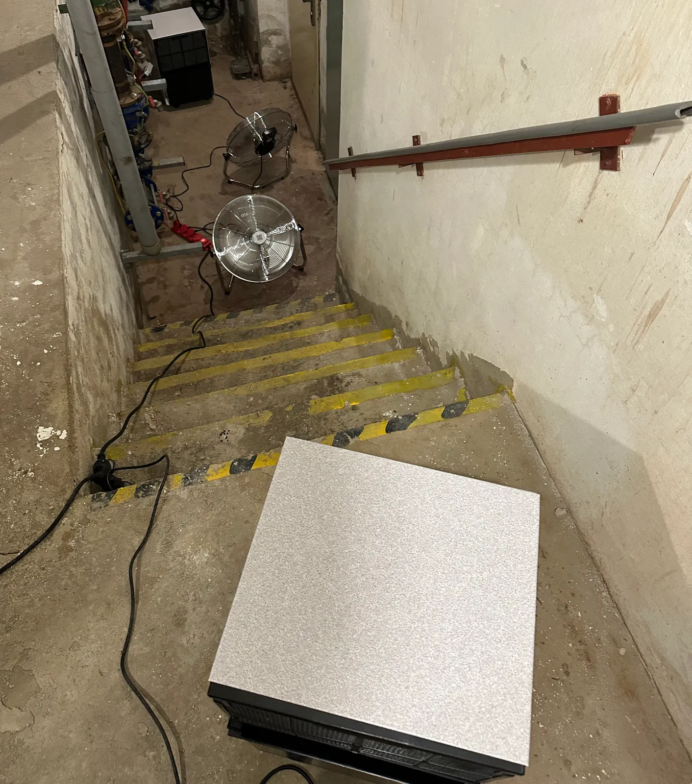 Kondenzační vysoušeč v chodbě sklepa a ventilátory u schodů do spodní úrovně.