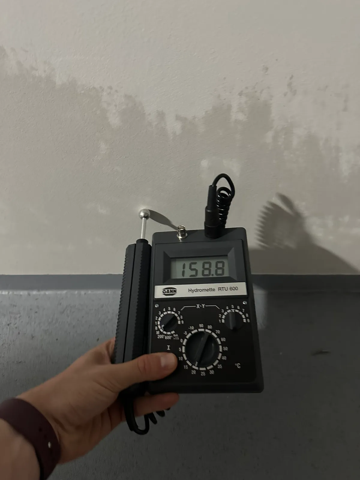 Technik měří vlhkost zdiva nad soklem, na omítce je vlhká mapa.