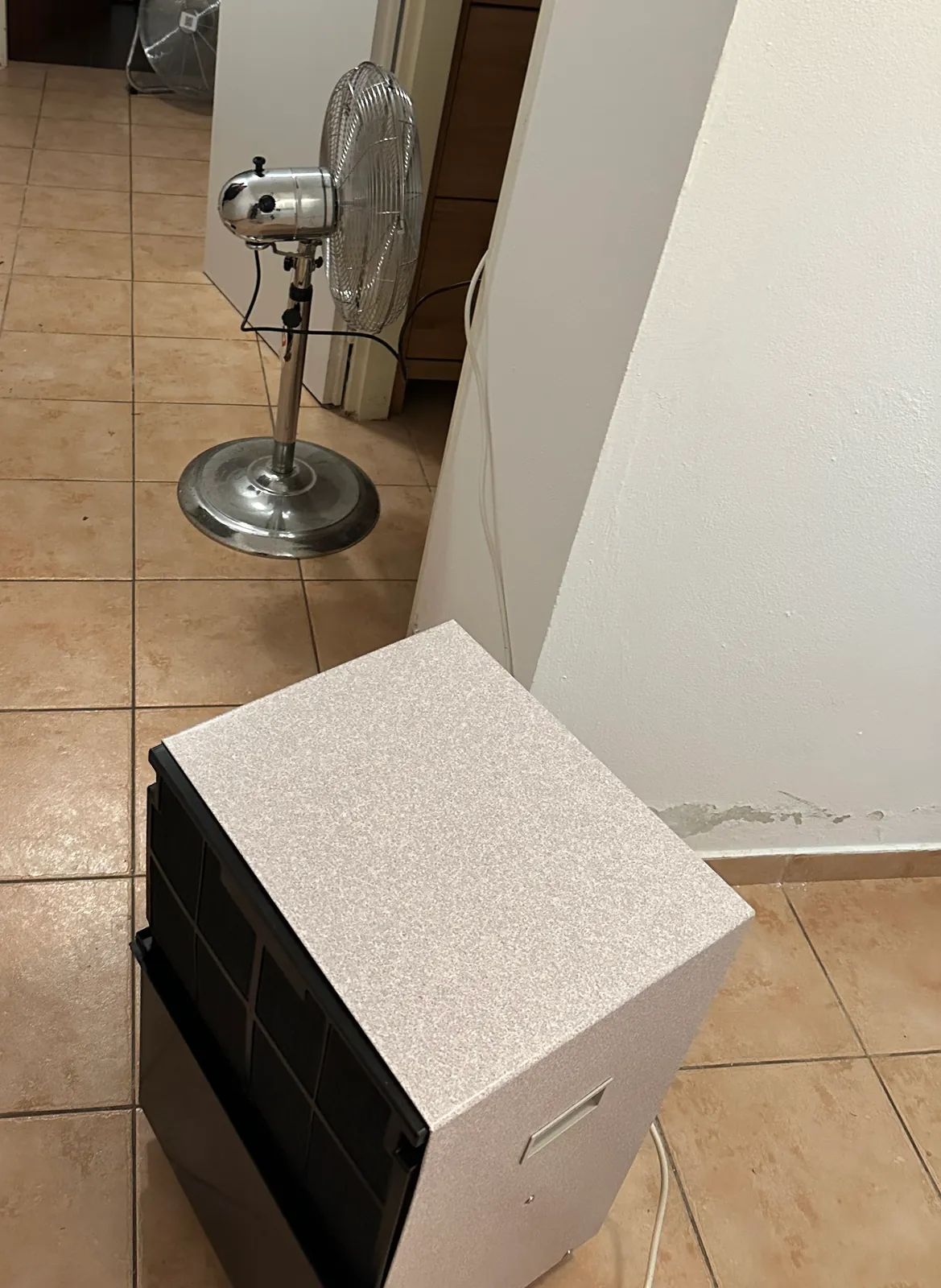Kondenzační vysoušeč a stojanový ventilátor v chodbě suterénu.